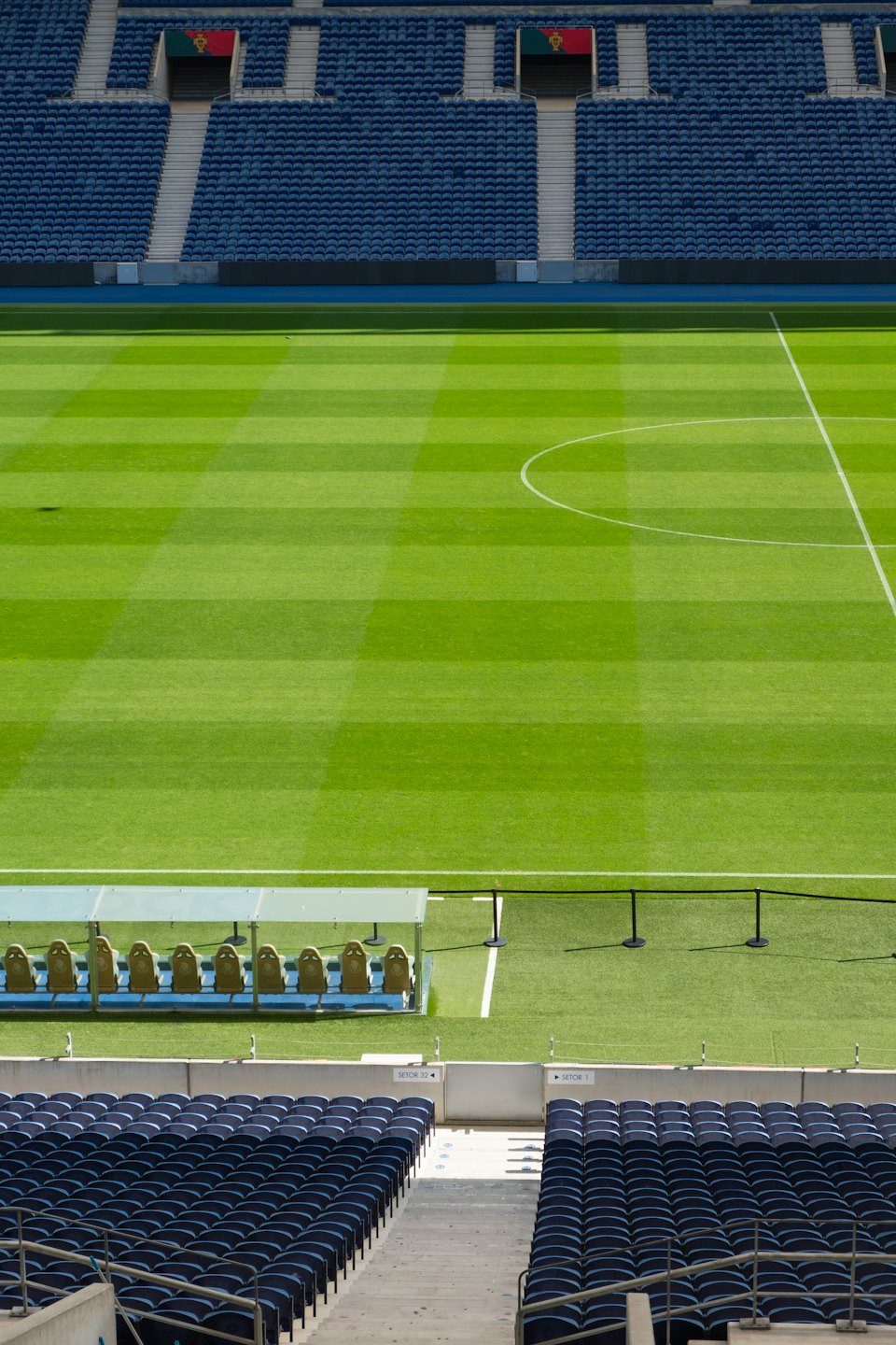 Empty sports stadium with vibrant green football pitch and blue seats.